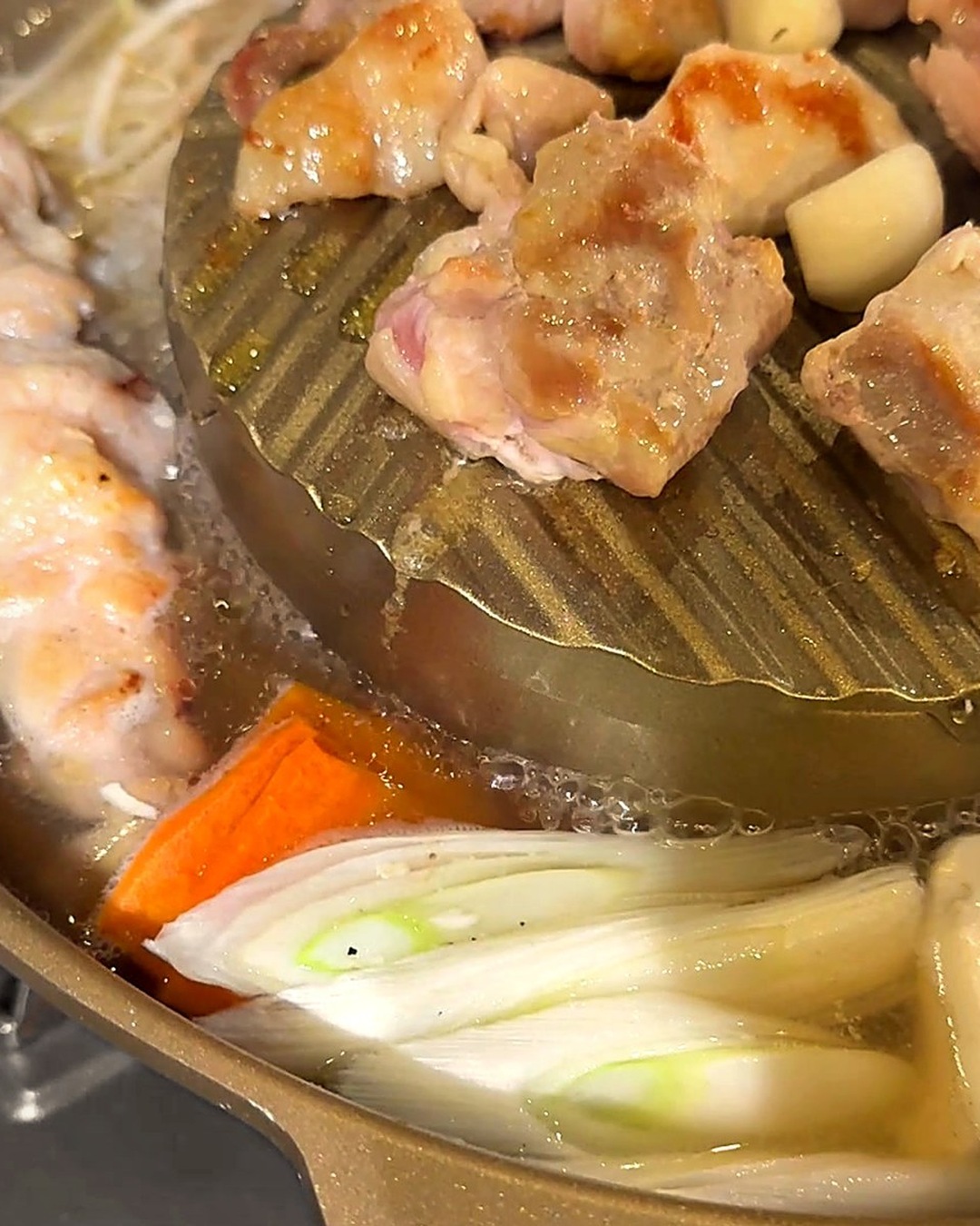 鍋の真ん中の鉄板で鶏肉とにんにくを焼き、まわりのスープでにんじんやねぎを煮ている様子